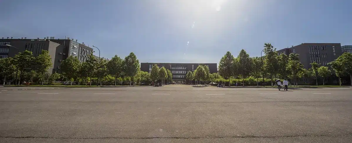 A blurred crowd of anonymous tech workers walking through a glass-walled campus corridor, heads down, phones in hand, conveying industry-wide unease