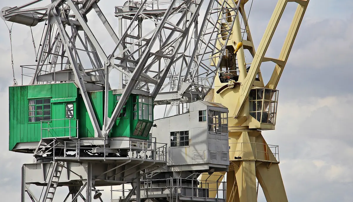 An aerial view of an oil tanker at a port facility, cargo being loaded or unloaded, industrial cranes in motion, symbolizing energy trade between nations