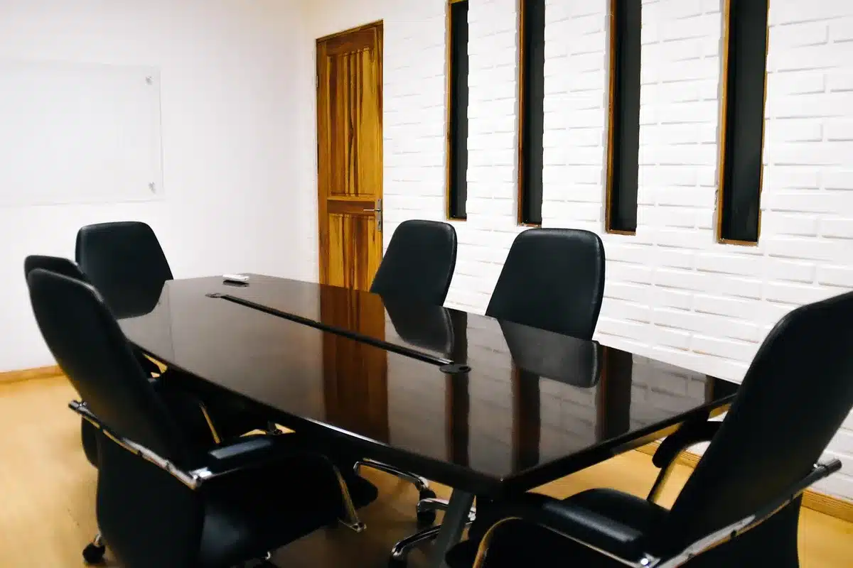 An empty diplomat's chair at a polished conference table, a single red telephone in the background, harsh overhead lighting casting sharp shadows, papers and a water glass visible, the room austere and silent.