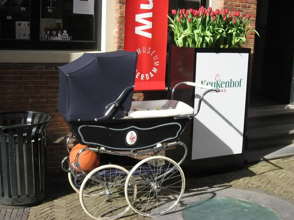 An empty residential street at dawn outside a generic townhouse, a stroller parked on the pavement under a streetlamp, no people visible