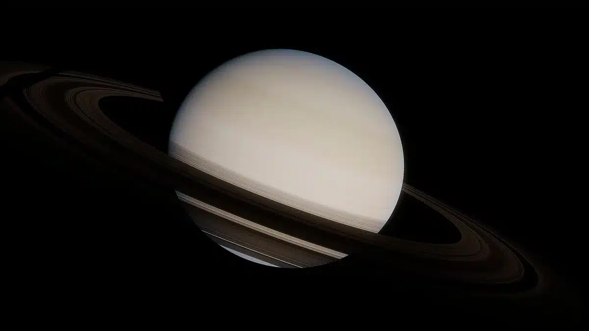 A close-up false-color Hubble image of Saturn's south pole showing the decagon wave marked by an arrow, with concentric latitude circles visible and the wave's fuzzy, evolving edges distinct from the stable north pole hexagon
