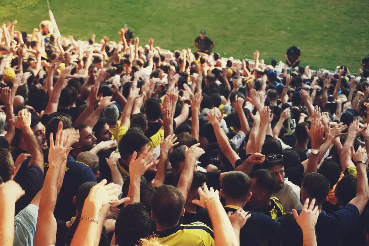 Wide shot of anonymous crowd in a college stadium reacting with arms raised, motion blur under floodlights