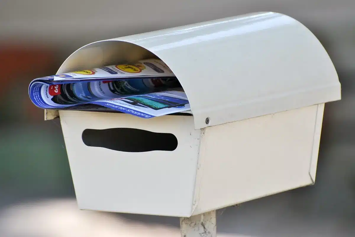 Empty mailbox on a porch with a stack of generic benefit notices visible inside, autumn light, anonymous setting
