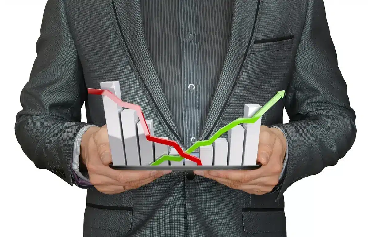 A close-up of a computer screen displaying an upward-trending inflation chart with red and blue lines, a pen pointing to recent data points, and a blurred calculator in the background.