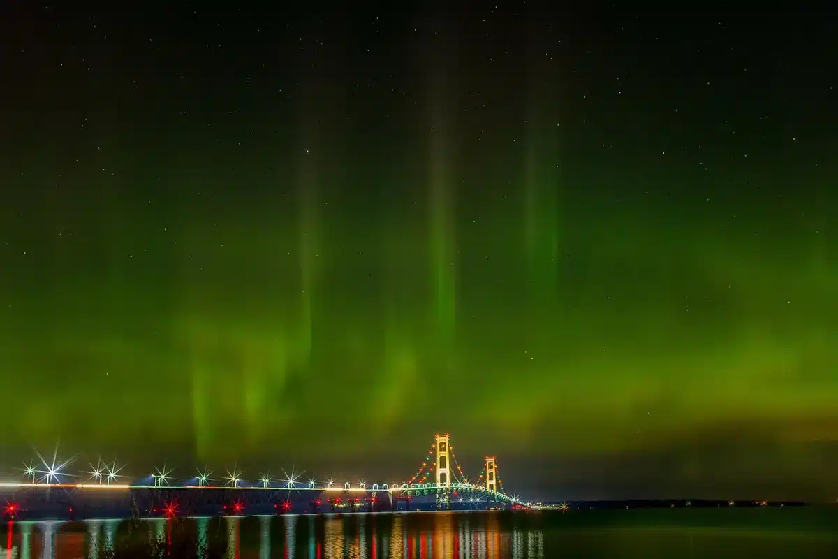 Northern lights aurora borealis dancing across night sky in green and purple waves over a landscape with silhouetted trees