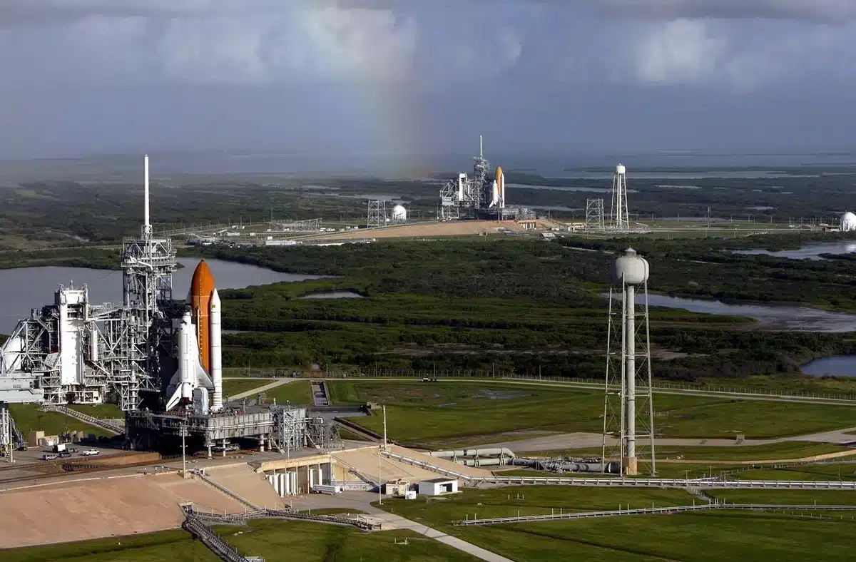 Empty launch viewing area at dawn with distant rocket silhouette, pylons and service structures visible, no logos or people