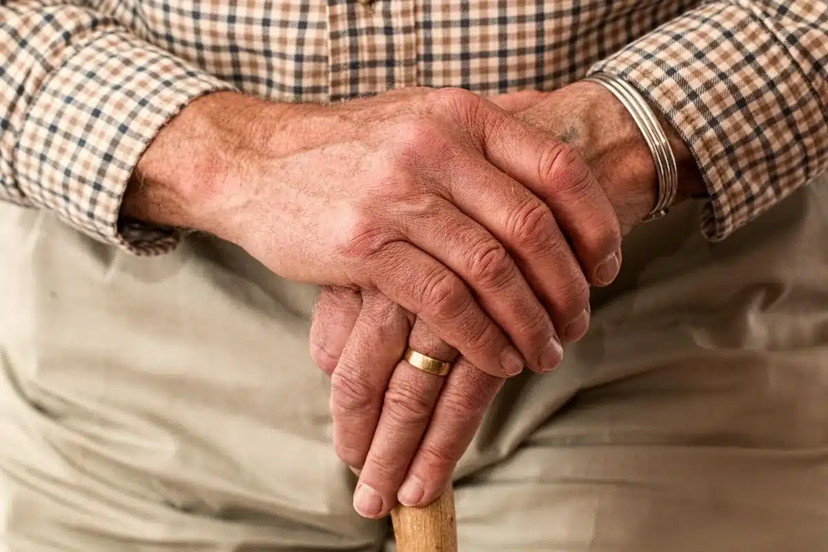 An older adult's hands holding bills and coins on a wooden table, suggesting financial planning or budgeting