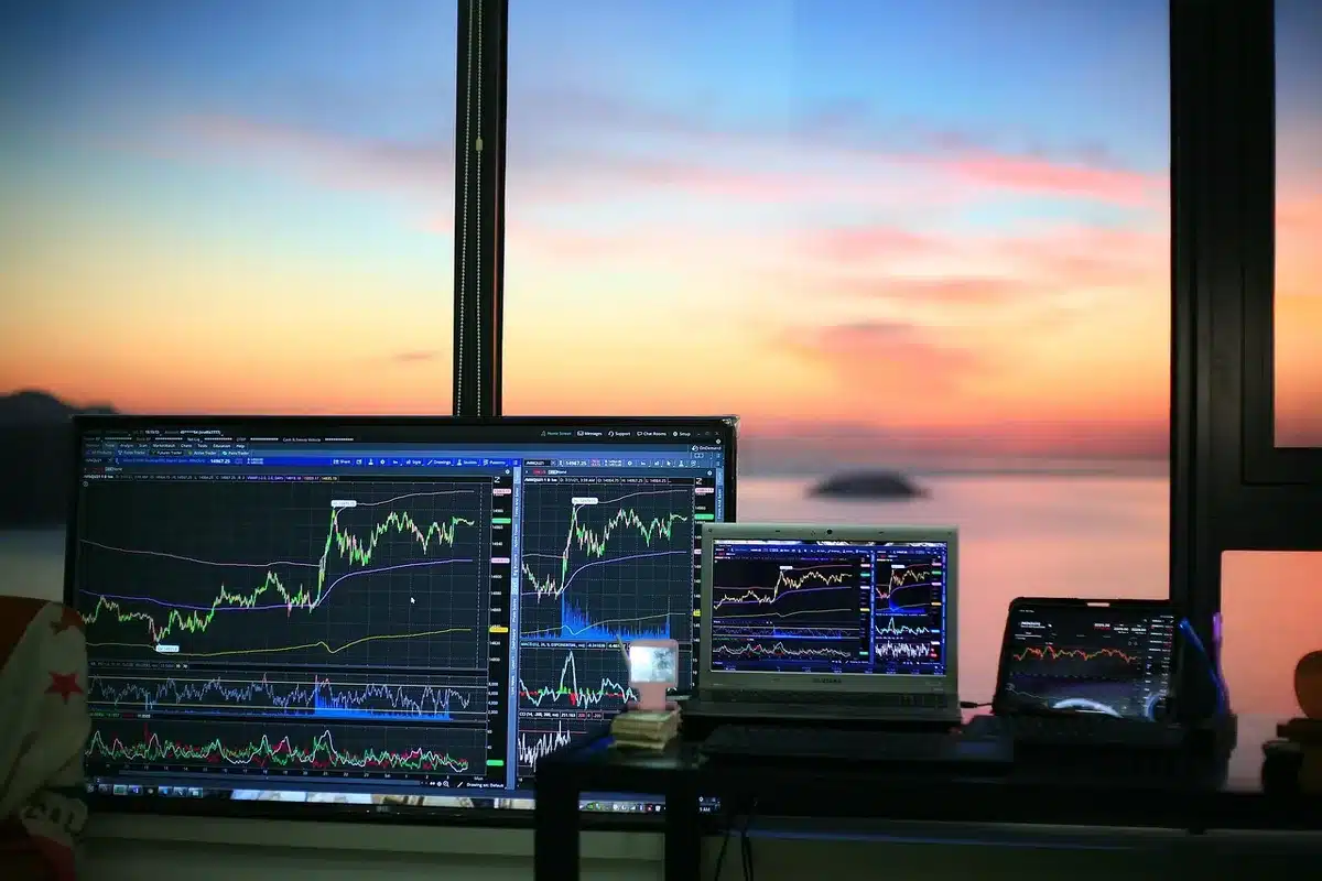 Close-up of anonymous hands on a laptop keyboard with a partial view of a candlestick chart on screen and a coffee cup nearby, suggesting late-night market monitoring — tension