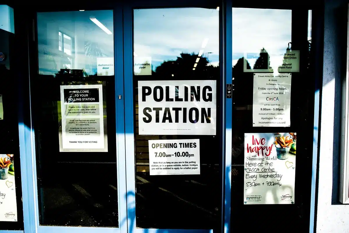 anonymous crowd outside a polling station at dusk, small groups chatting, flags not visible, blurred faces, papers and signage indistinct