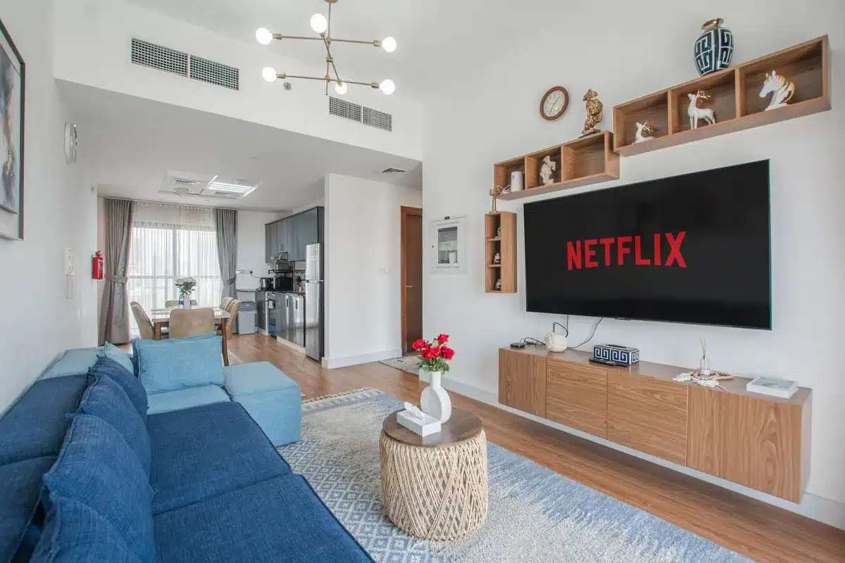 Empty late-night living room with a muted TV on, a remote on a coffee table and a folded movie magazine nearby; anonymous, no faces
