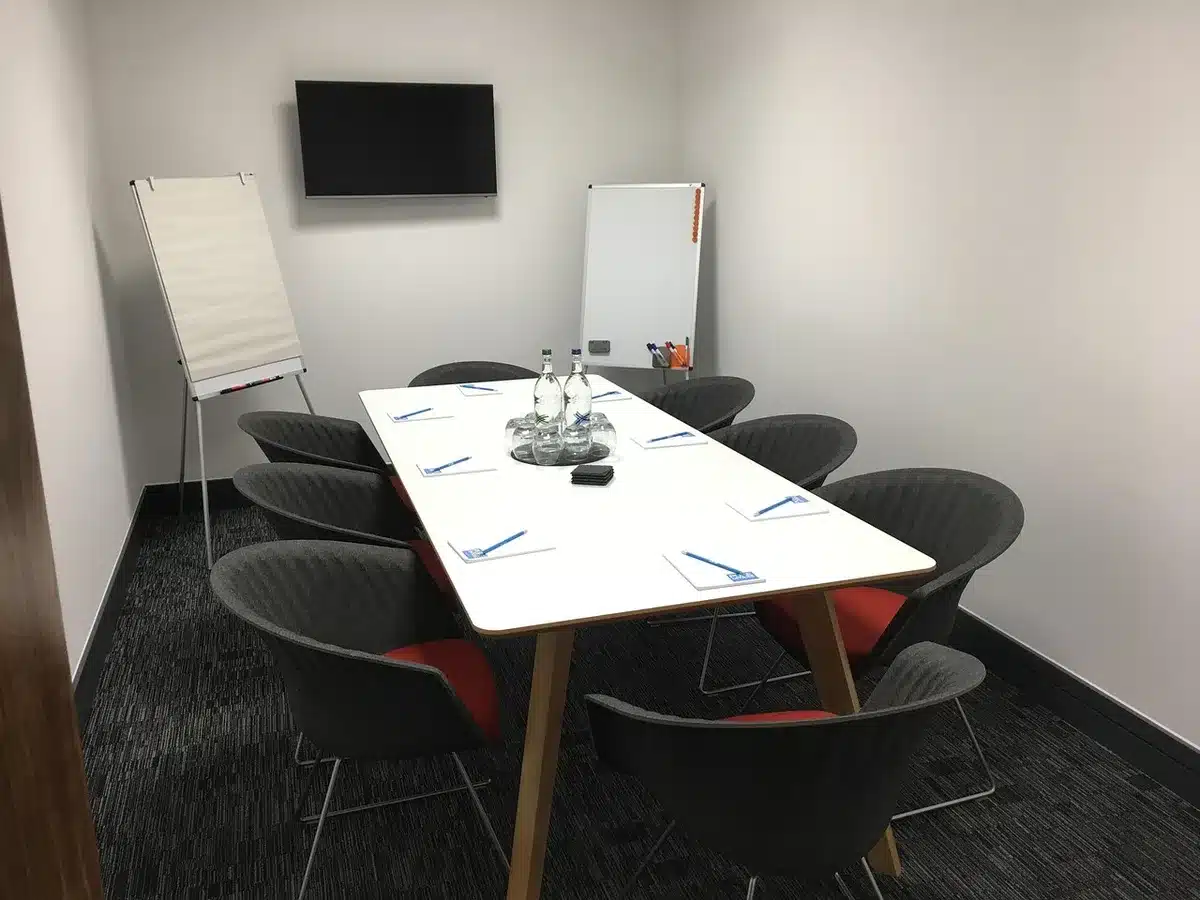 empty conference room with a long table and anonymous chairs, a single laptop open to a generic finance dashboard, soft morning light through blinds