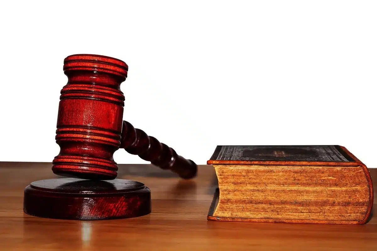 A gavel resting on a wooden judge's bench, law books stacked beside it, a single spotlight illuminating the gavel, the courtroom bench empty and silent