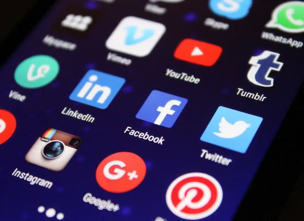 A crowded social media feed with trending hashtags and conspiracy theories scrolling rapidly, anonymous hands holding phones, neon blue and red light on faces, tension and urgency visible