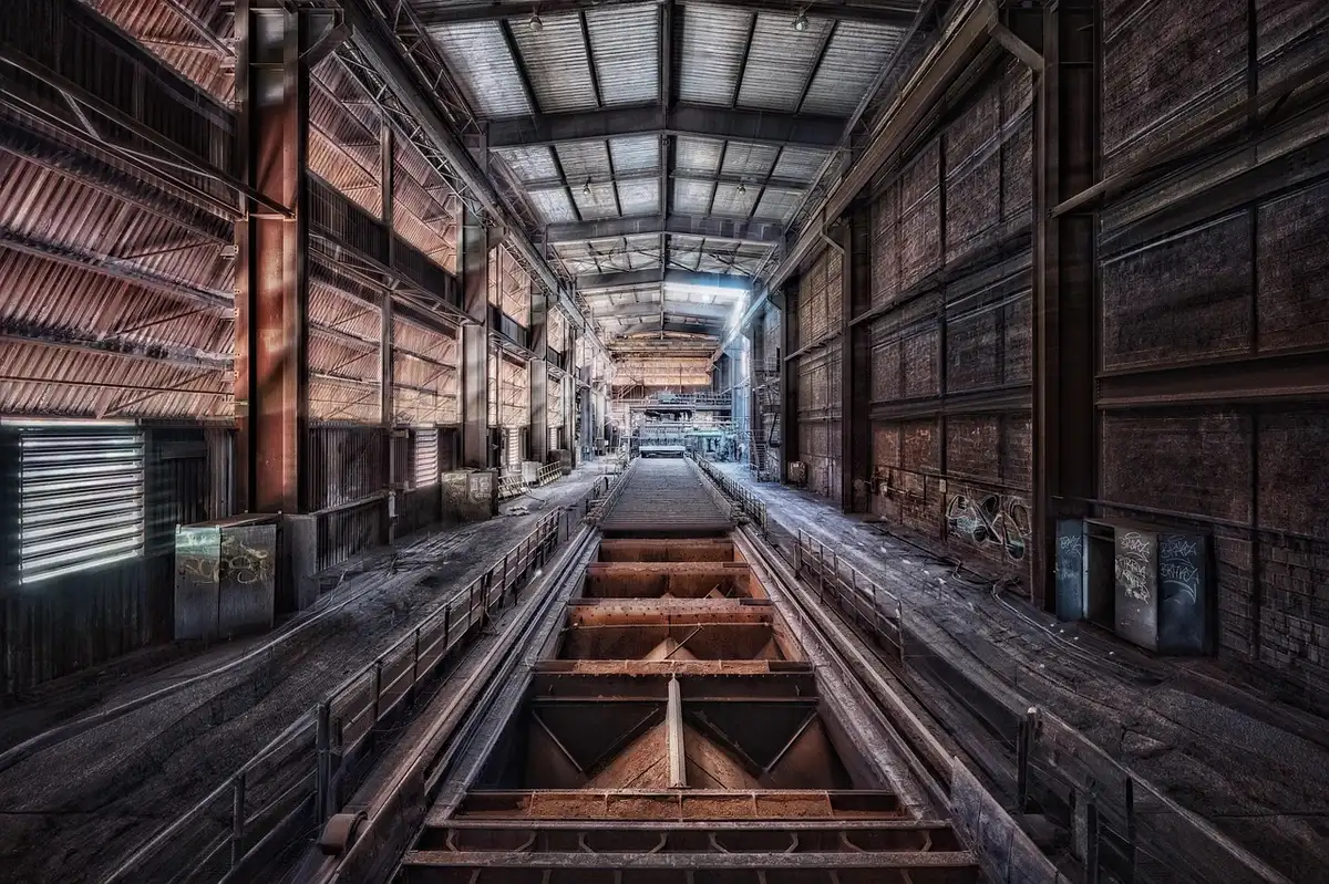 Anonymous silhouetted workers in a manufacturing plant with machinery and empty pallets in the foreground