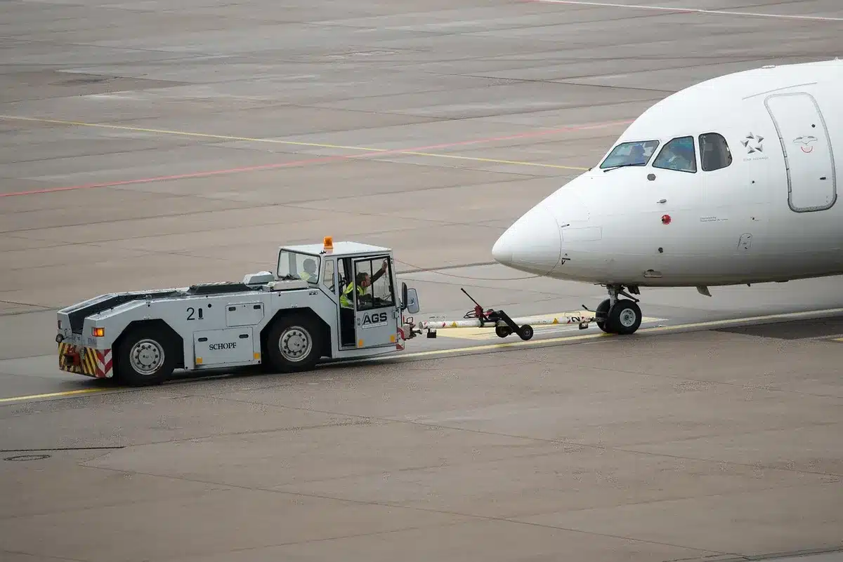 President stepping off aircraft with darker tousled hair, navy suit visible, tarmac and reporters in soft focus background, moment of arrival captured, public scrutiny evident
