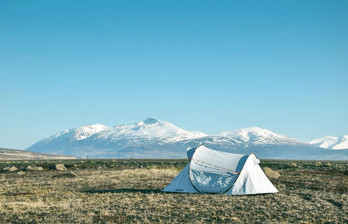 Wide view of a snow-blanketed shoreline and a military-style tent camp being set up, anonymous figures bundled against wind, equipment crates visible but unbranded
