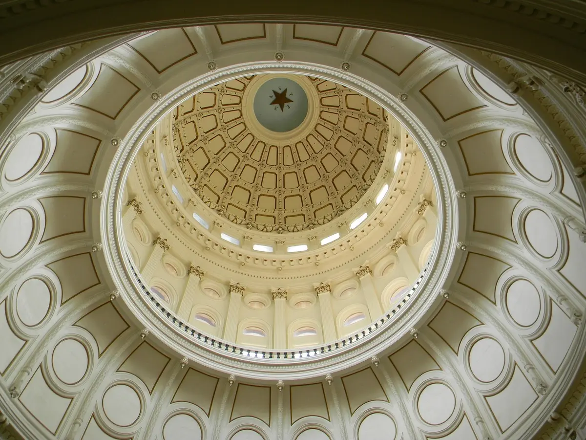 Silhouette of a governor or state official speaking at a podium, looking resolute against a blurred state capitol building backdrop, warm interior lighting