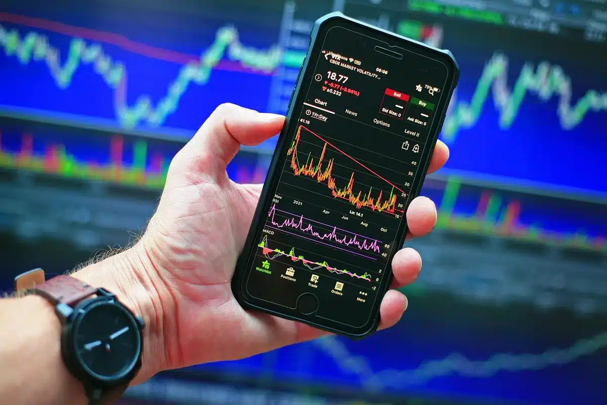 Anonymous hands holding a smartphone showing a generic polling graph with red and blue bars blurred, a coffee cup and notebook at the edge of the frame