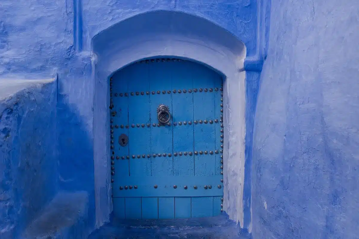 A closed ornate door in dim hallway lighting, with a single spotlight beam creating a sense of uncertainty and waiting