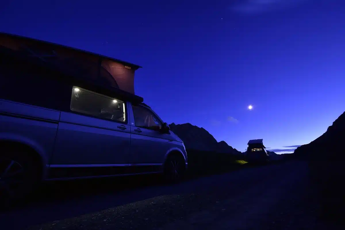 A small group of anonymous TV news vans parked outside a government building at dusk, satellite dishes stowed, crews absent