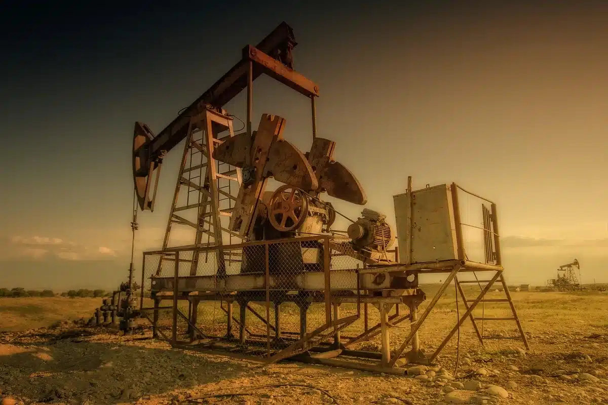 An industrial oil extraction facility with steel drilling derricks silhouetted against a twilight sky, Venezuelan landscape in the background, emphasizing scale and infrastructure investment