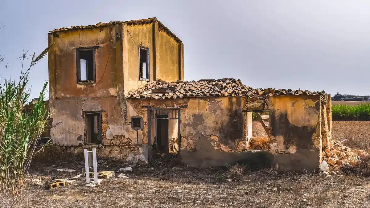 Damaged building with rubble and gaping hole in roof, twisted metal, debris scattered around, gray concrete dust settling in air.