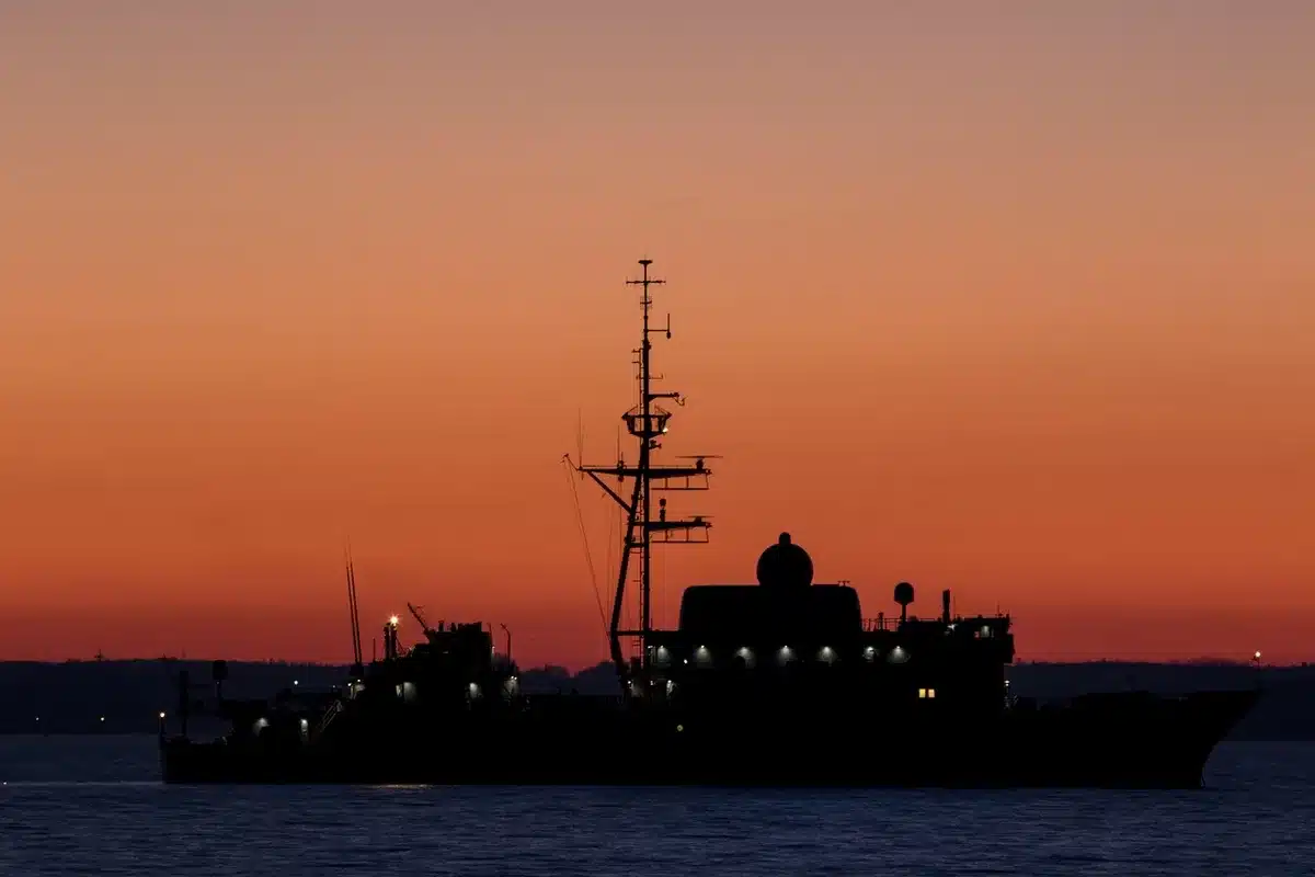 Three military warships silhouetted against a dawn horizon on open ocean, missile contrails streaking across a gray sky, water churning from distant explosions, tension and precision converging