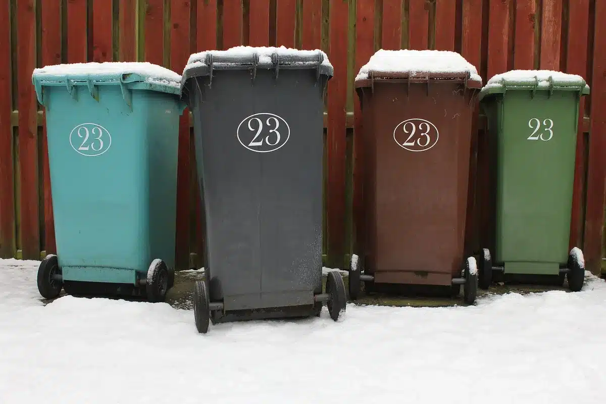 A row of anonymous blue USPS-style collection bins at dusk beside a church parking lot, one bin lid open with scattered envelopes on the pavement, no visible logos or people