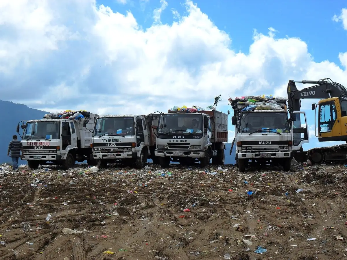 A modern waste management facility with automated sorting equipment and conveyor systems, workers in safety gear monitoring operations, bins and recycled materials moving through the facility