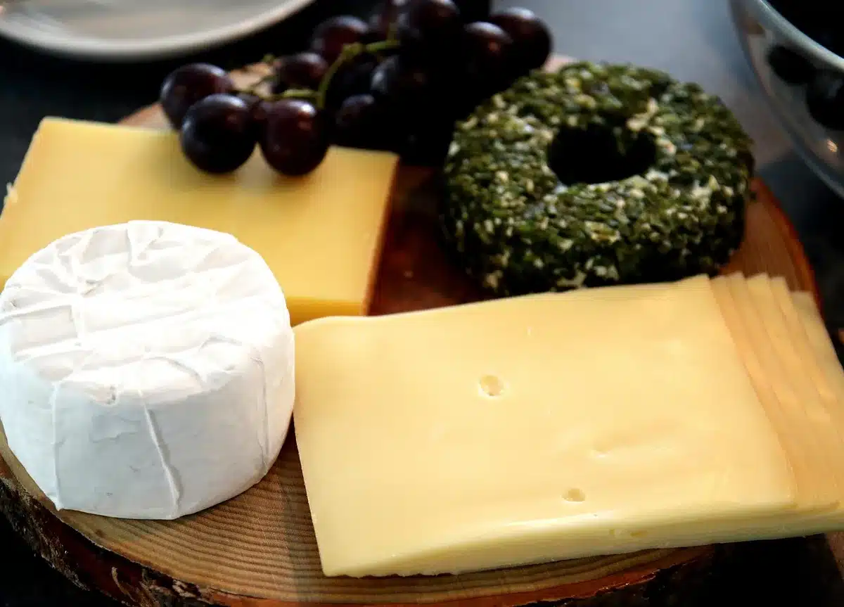 An anonymous empty supermarket cheese counter with several unbranded cut cheese wedges on white paper, a blank scale label nearby and a blurred aisle in the background