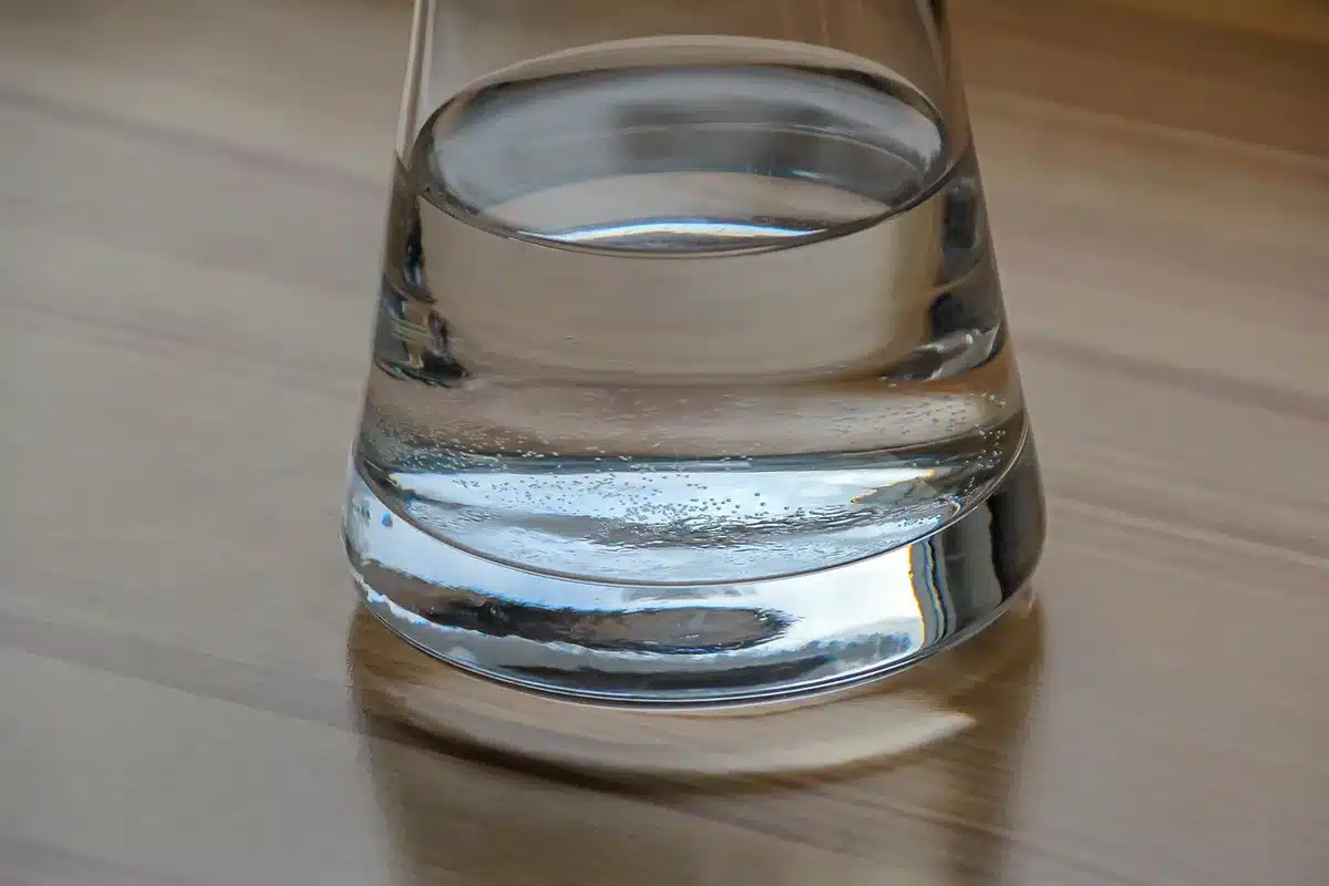 An empty kitchen sink with a running faucet, a single glass and a small pot on the stove; no people, no brands visible, a roll of paper towels nearby