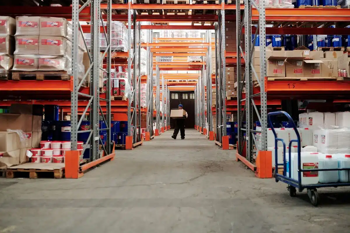 A generic fulfillment-hub warehouse aisle, stacked pallets and an empty trolley under industrial lights; no company branding