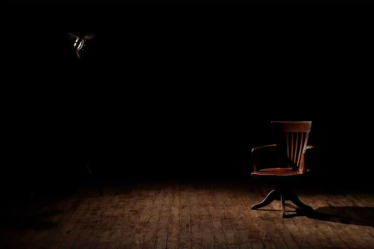 Wide, empty conference stage with a single lectern under a spotlight and a blank projection screen behind it, suggesting a pending corporate announcement