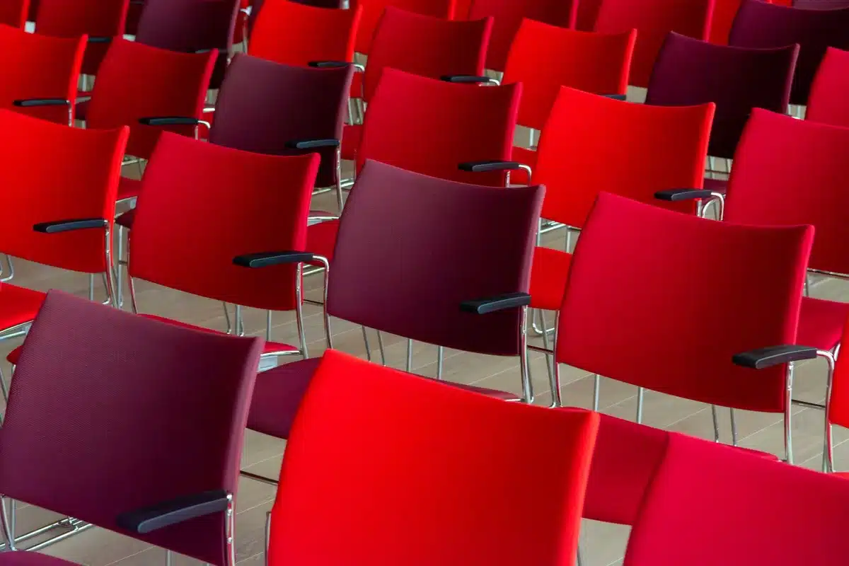 A plain convention center breakout room with an empty stage, a moderator's chair, a small round table and three water glasses; no people, banners or logos visible