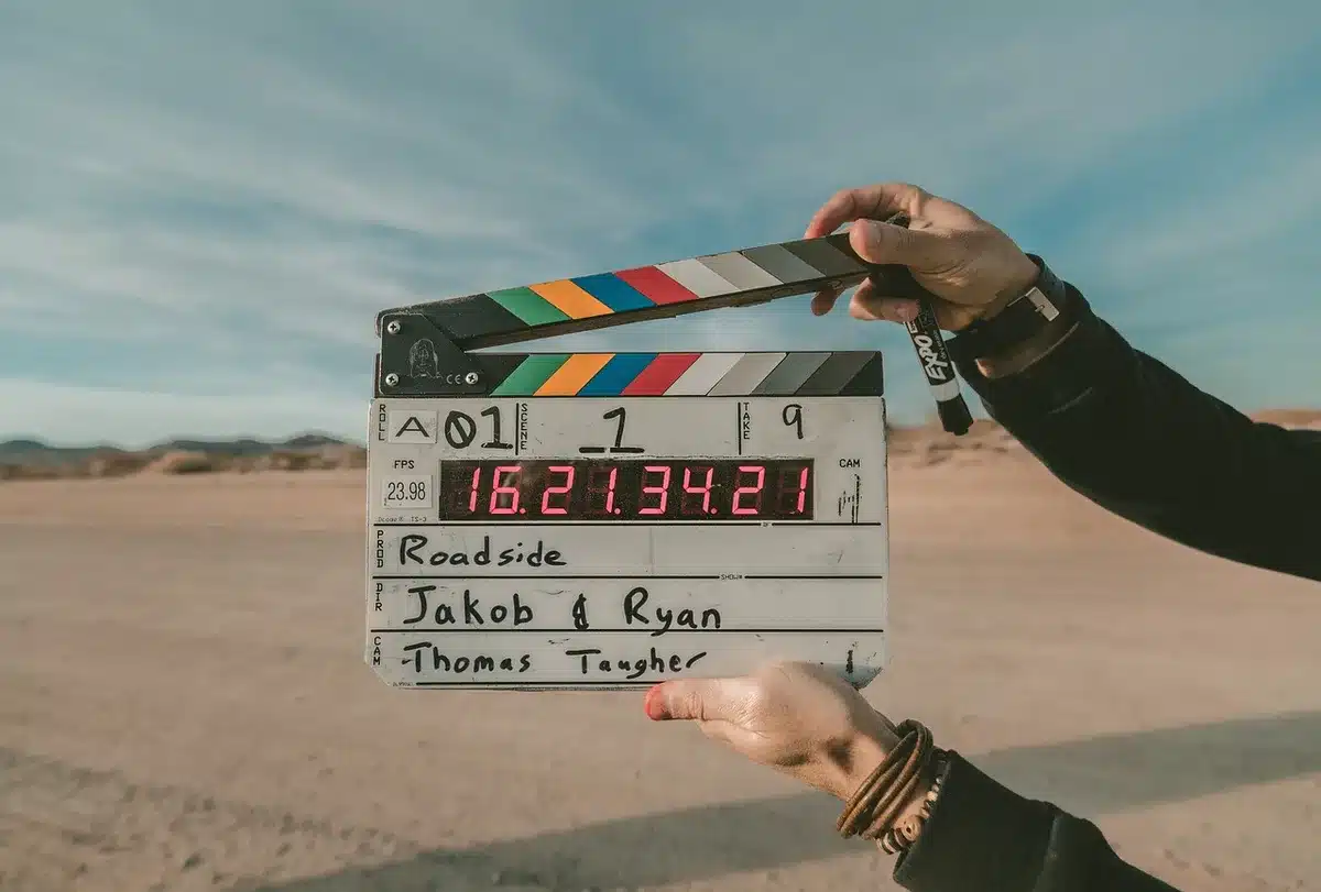 Close-up of a rolled film clapperboard on a table, hands off-frame, with a generic script page partially visible but unreadable