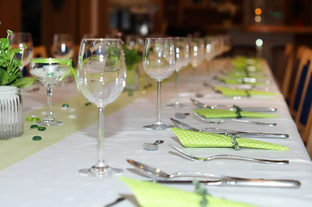 A dimly lit dining table set for a formal meal, empty plates and wine glasses arranged around a long table in a stately room
