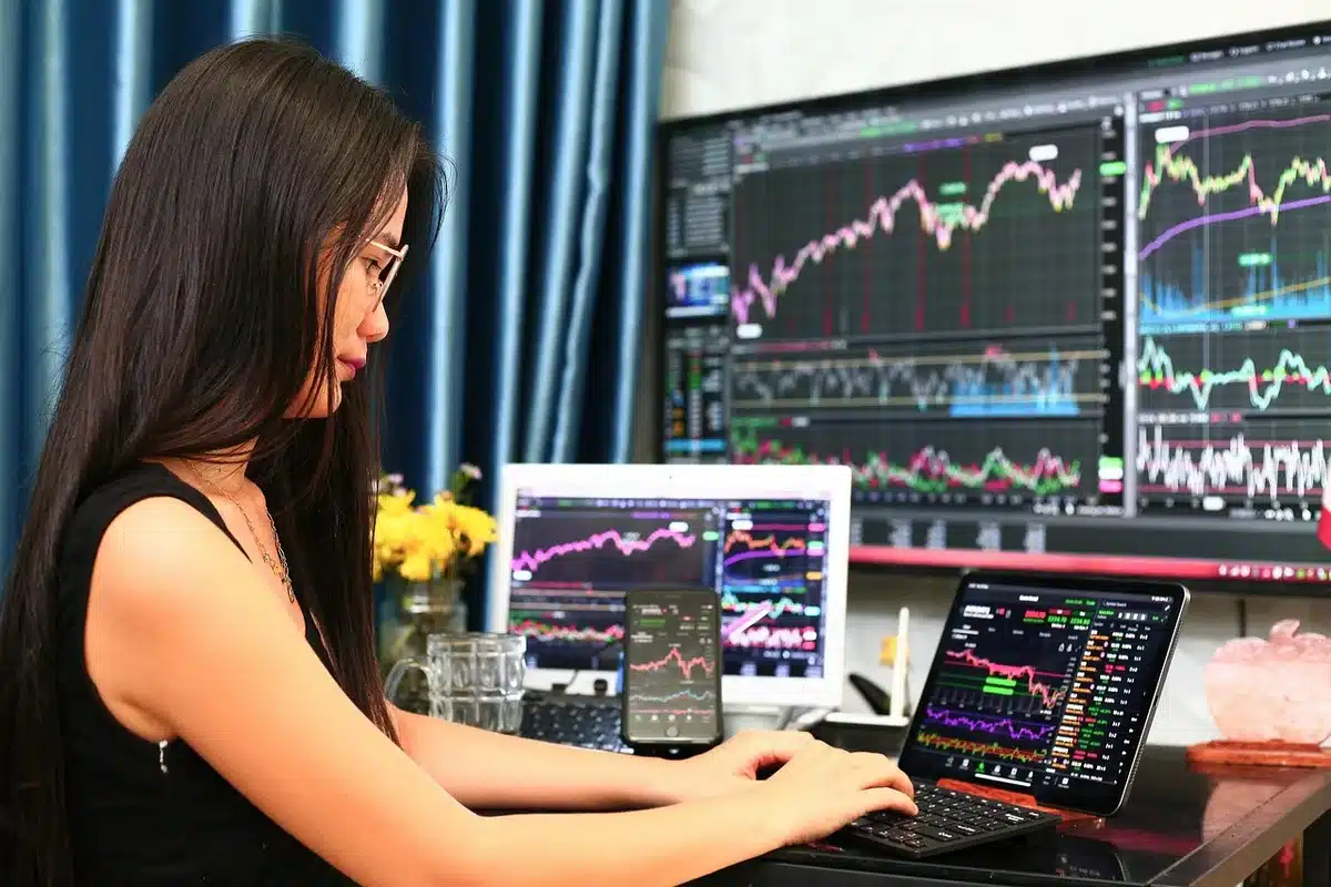Close view of an anonymous trader’s hands hovering over a laptop showing a red intraday stock chart and scattered printed bond yield tables on a desk