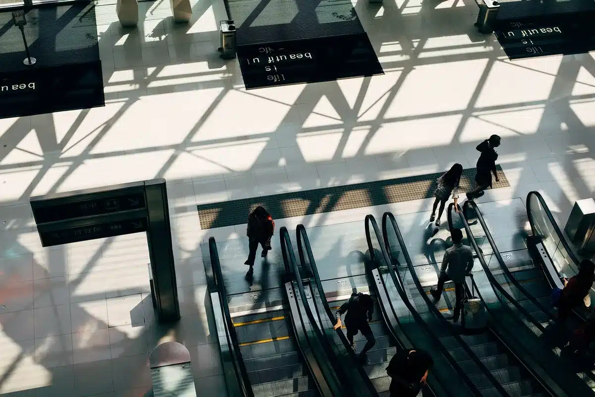 Empty airport concourse at dusk with a single unbranded jet at the gate, departure screens blurred and few anonymous travelers walking past — tension