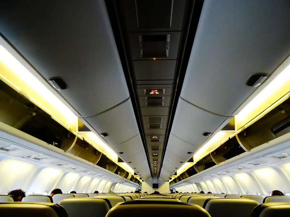 Cabin crew trolleys stowed, an empty economy cabin aisle lit by overhead lights; no logos, no faces visible, a lone service cart parked — quiet