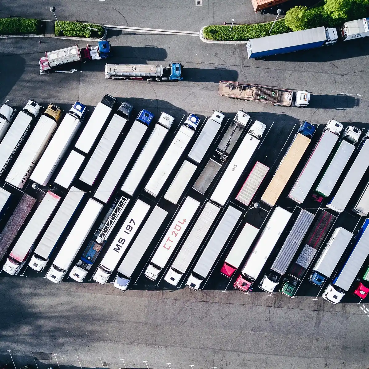 Wide-angle view of an anonymous fleet yard at dawn, several unbranded box trucks and one tractor lined up, a fuel tanker in the background