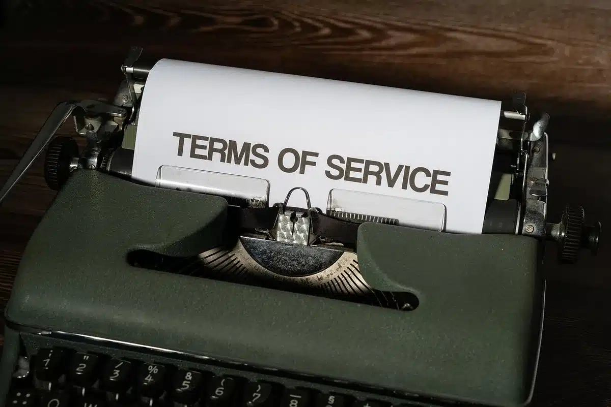 A lone stack of unbranded legal envelopes and a typed formal complaint resting on a plain wood table, a pair of reading glasses beside them, late-morning light across the paper