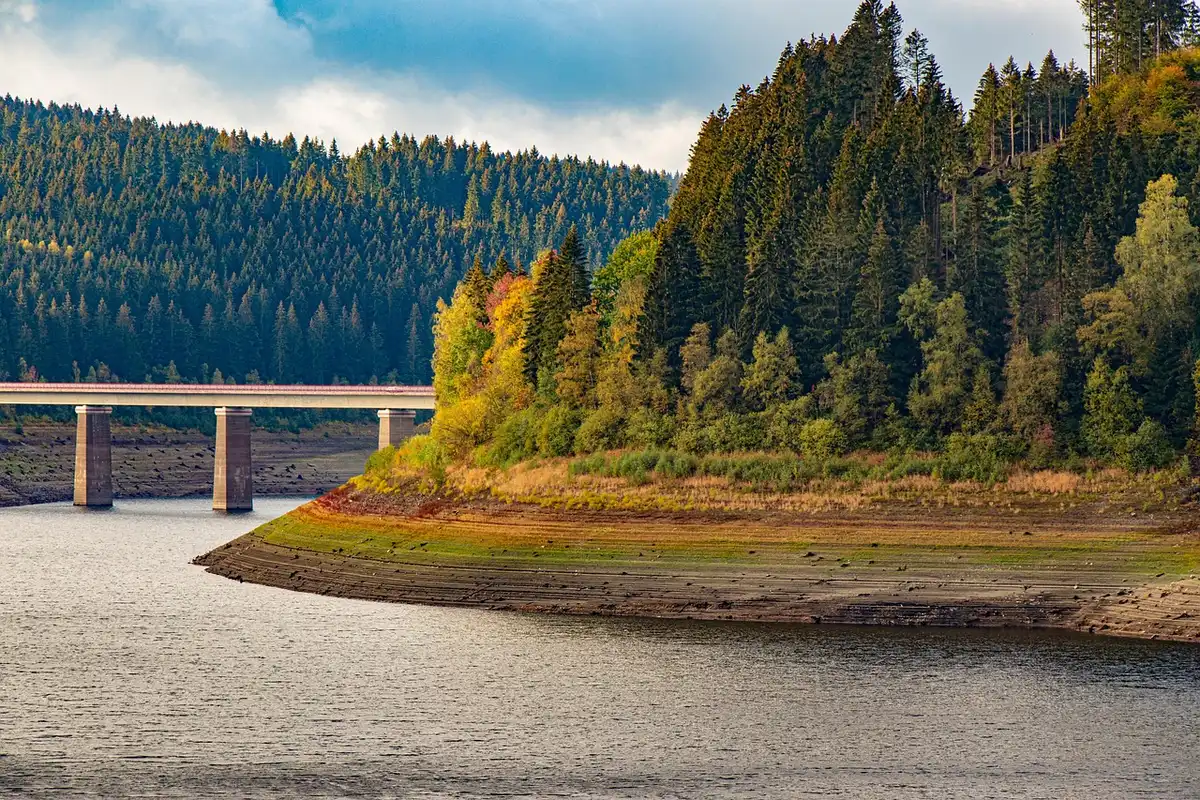 a long view of a dry concrete penstock entrance, empty and sunlit, hinting at low reservoir levels and exposed infrastructure