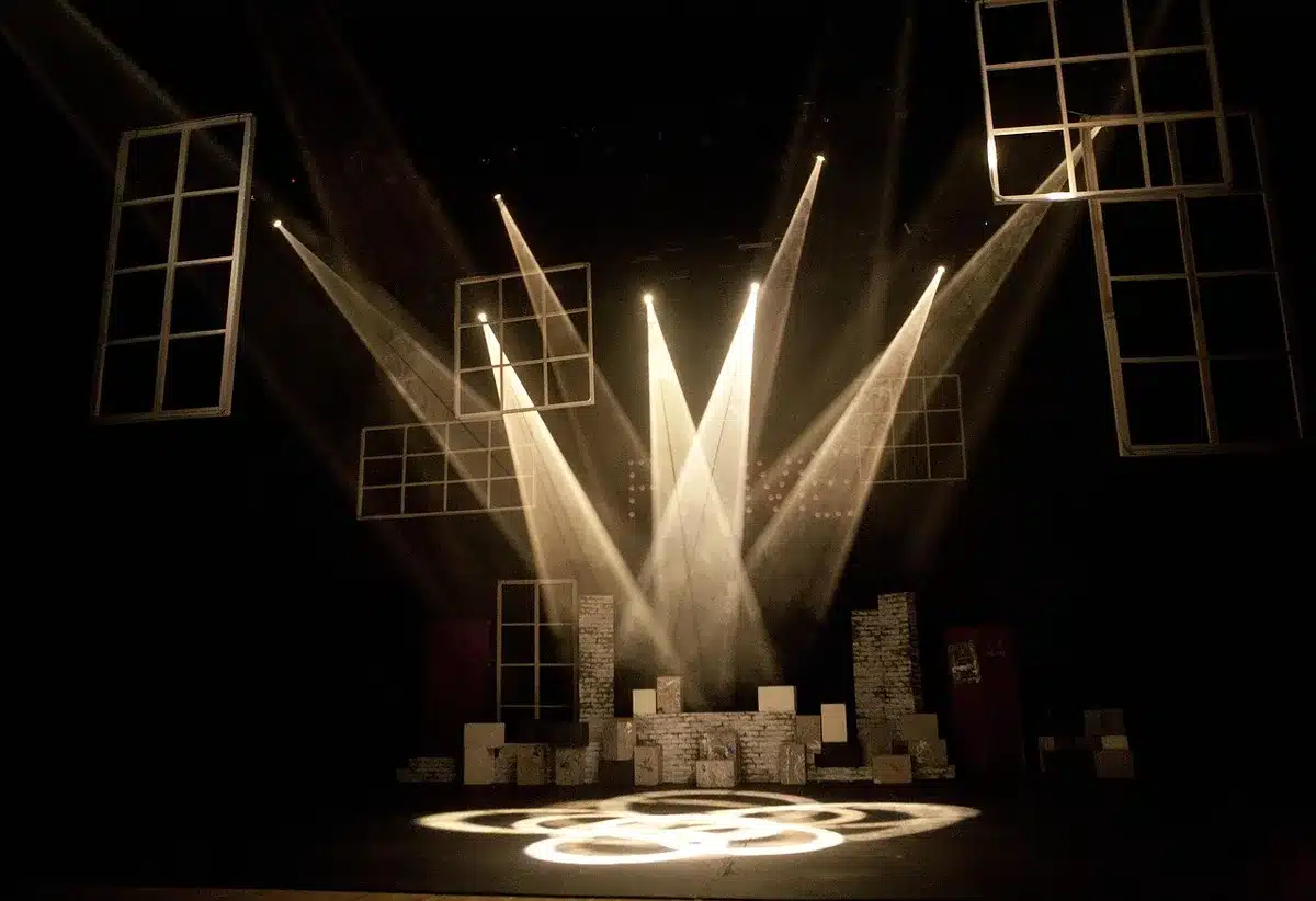 An empty stage framed by velvet curtains and warm spotlights, a single microphone on a stand center-stage with a folded setlist at its base, no people visible