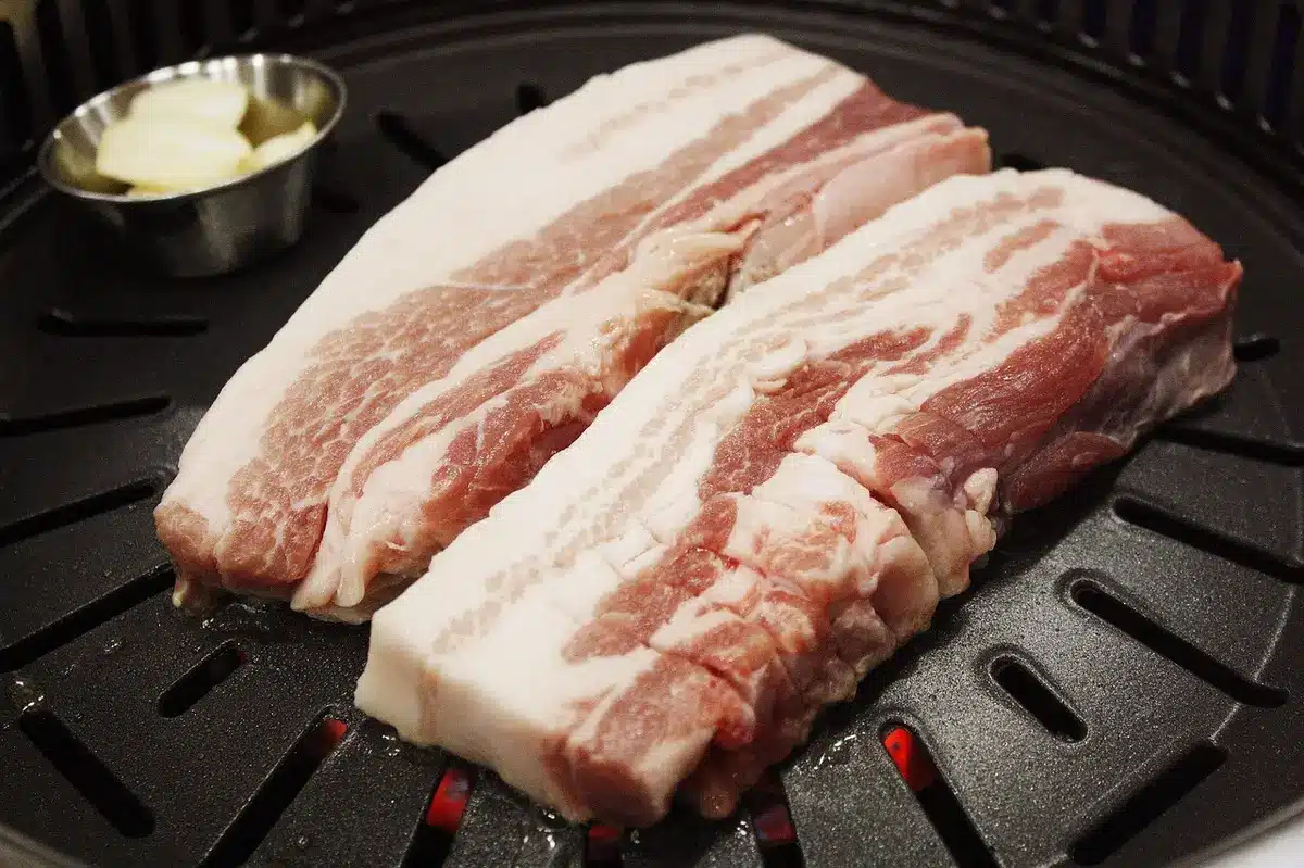 Close-up of several packaged, unbranded hot dogs and bacon in clear plastic trays on a plain table, UPC label area visible but unreadable