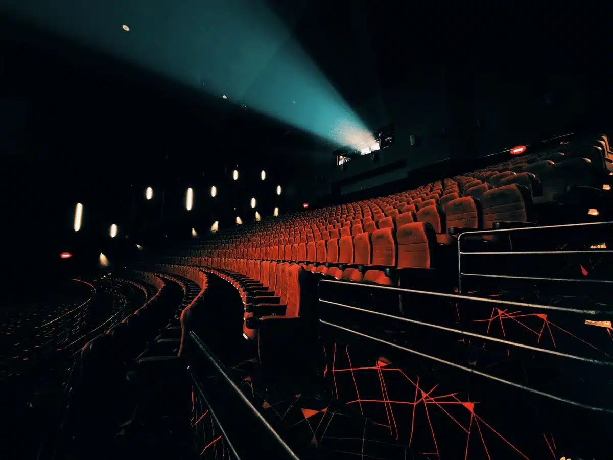 An empty performance hall with rows of unbranded seats, a dim stage light on the centre, and a single anonymous protest sign leaning against an aisle seat