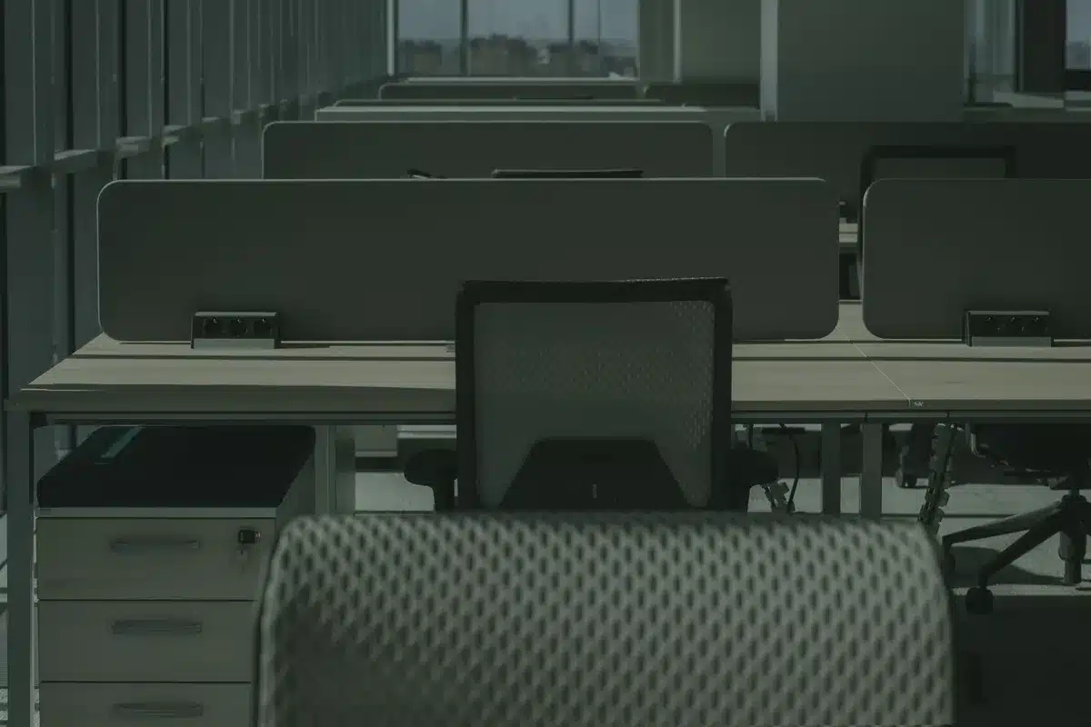 empty newsroom desk with folded broadsheet and a generic coffee cup; anonymous hands typing on a laptop in the background