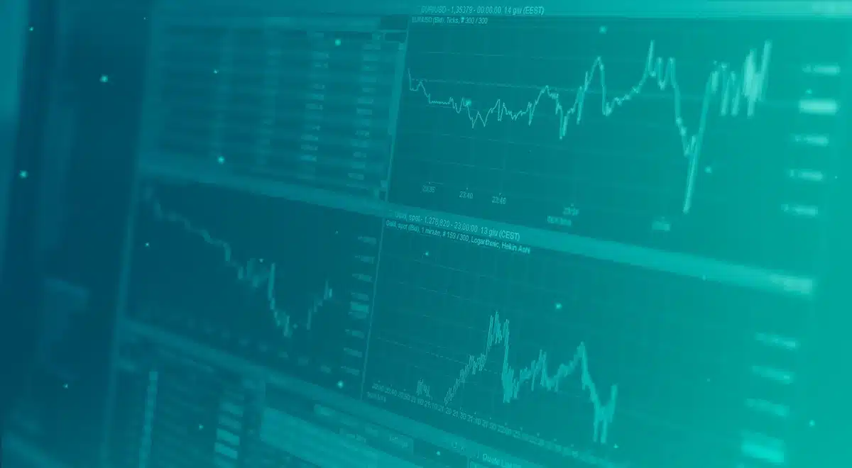 An empty trading desk with muted monitors showing blurred red and green line charts, a single coffee mug and scattered paper notes suggesting active trading but subdued activity