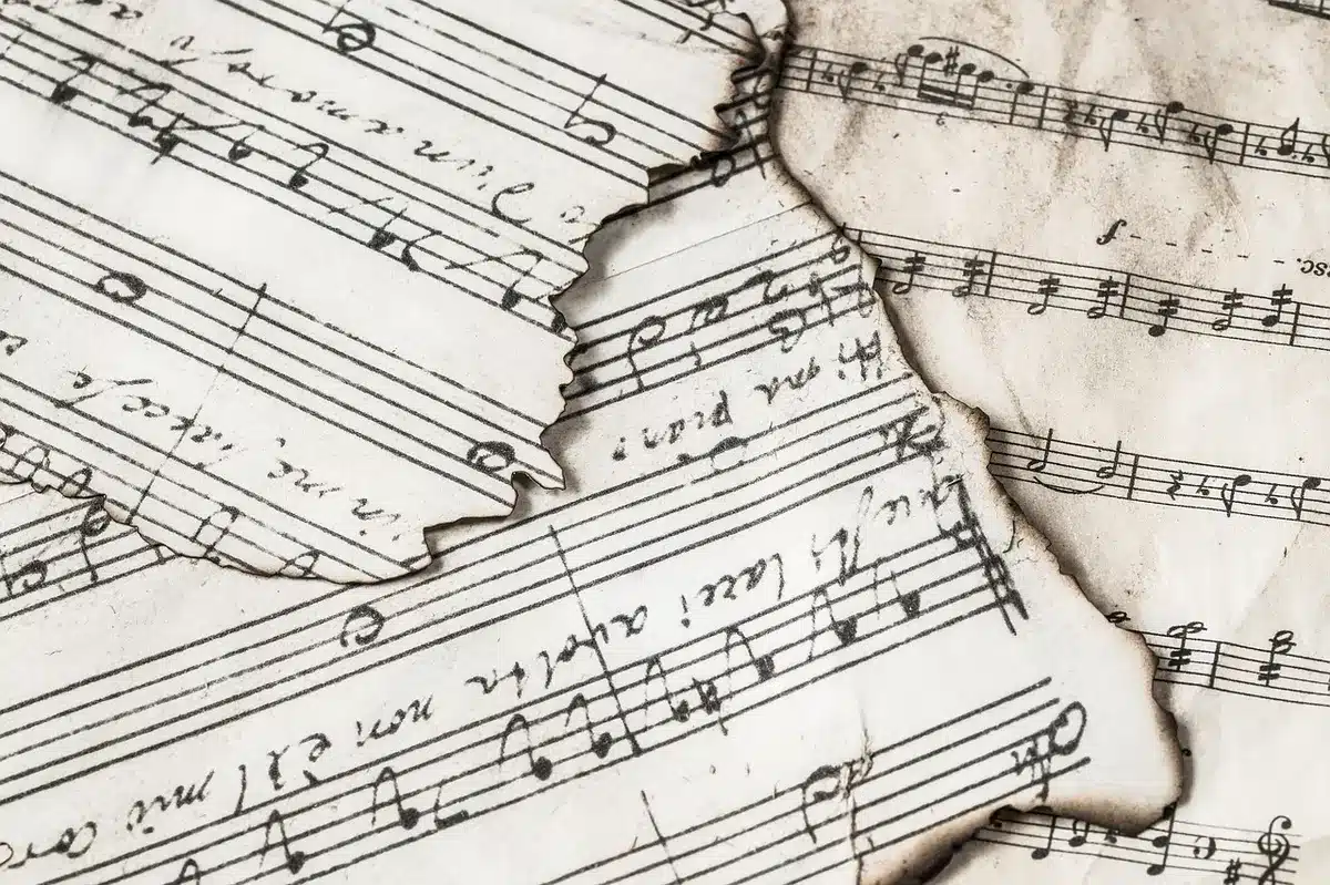 A close-up of sheet music and an orchestral conductor's baton lying on a rehearsal stand, pages slightly worn