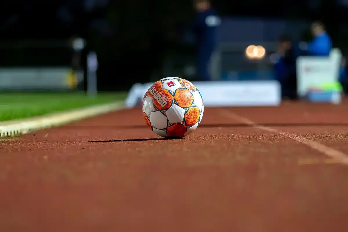 Wide shot of an empty stadium tunnel and a glistening pitch under floodlights, a single abandoned football boot near the touchline