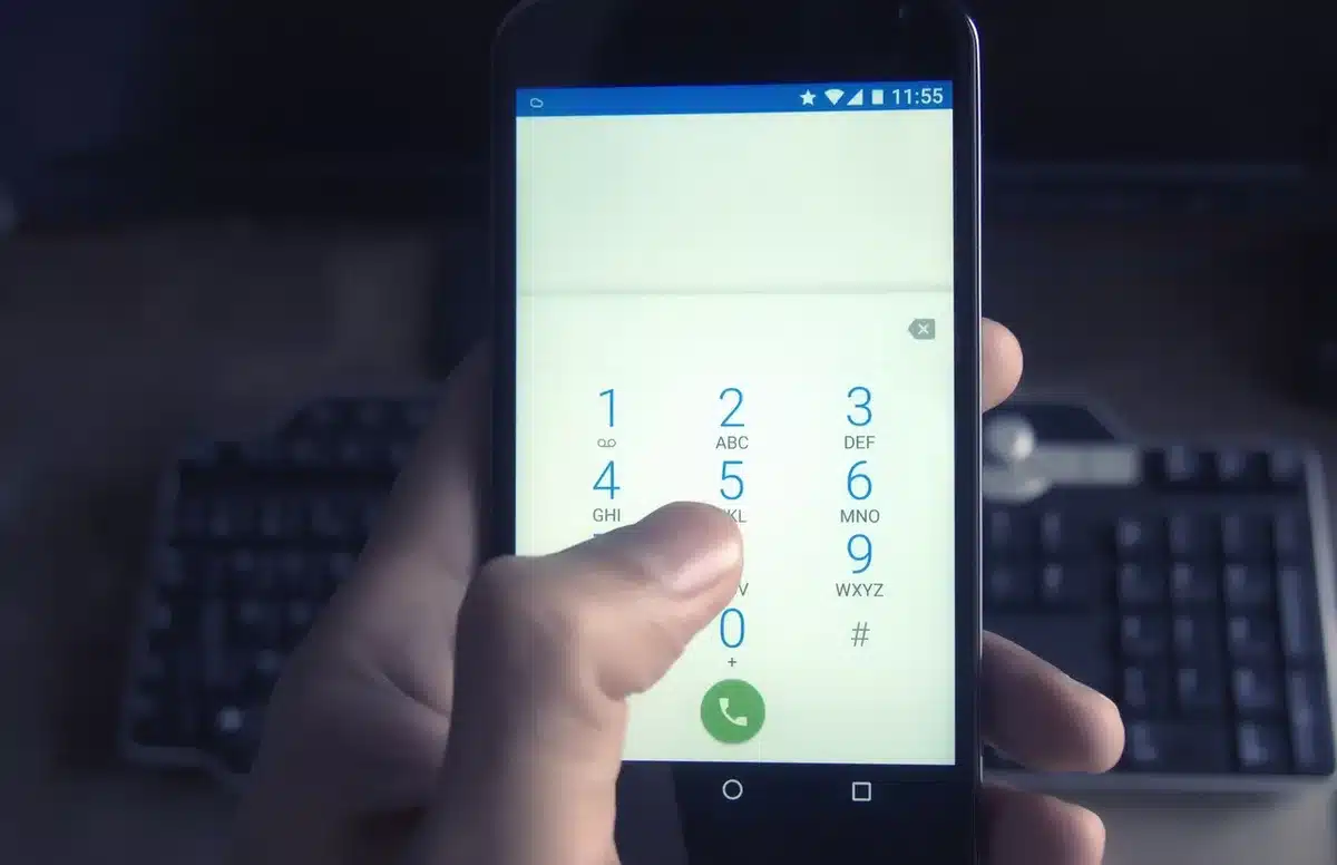 An anonymous pair of hands holding a smartphone showing a ringing call screen next to a blurred street scene, phone number not readable